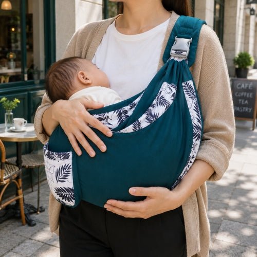 Porte-bébé à une épaule bleu pétrole avec poche intégrée et boucle réglable, position horizontale près d’un café
