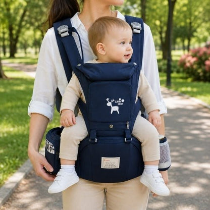 Porte-bébé avec capuche bleu marine, panneau ouvrable et rangements, porté face vers l’avant dans un parc