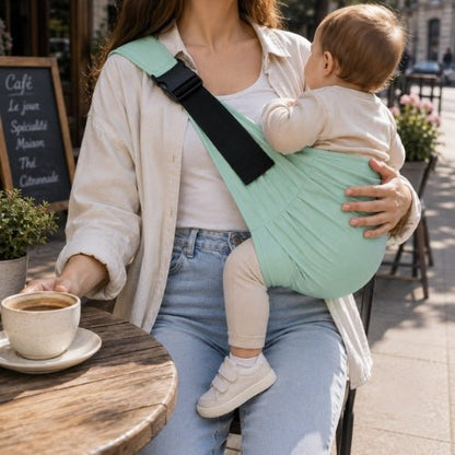 Bandouliere porte bebe vert menthe avec boucle réglable, port latéral près d’un café