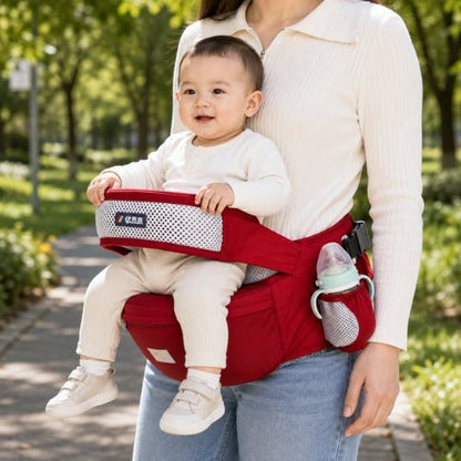 Porte bebe cote hanche rouge avec siège large et porte-biberon latéral dans un parc