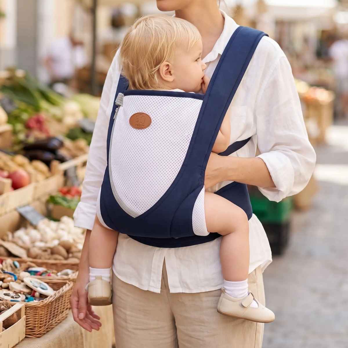 Porte-bébé croisé dans le dos bleu marine avec bretelles larges et panneau en maille, porté face au porteur dans un marché
