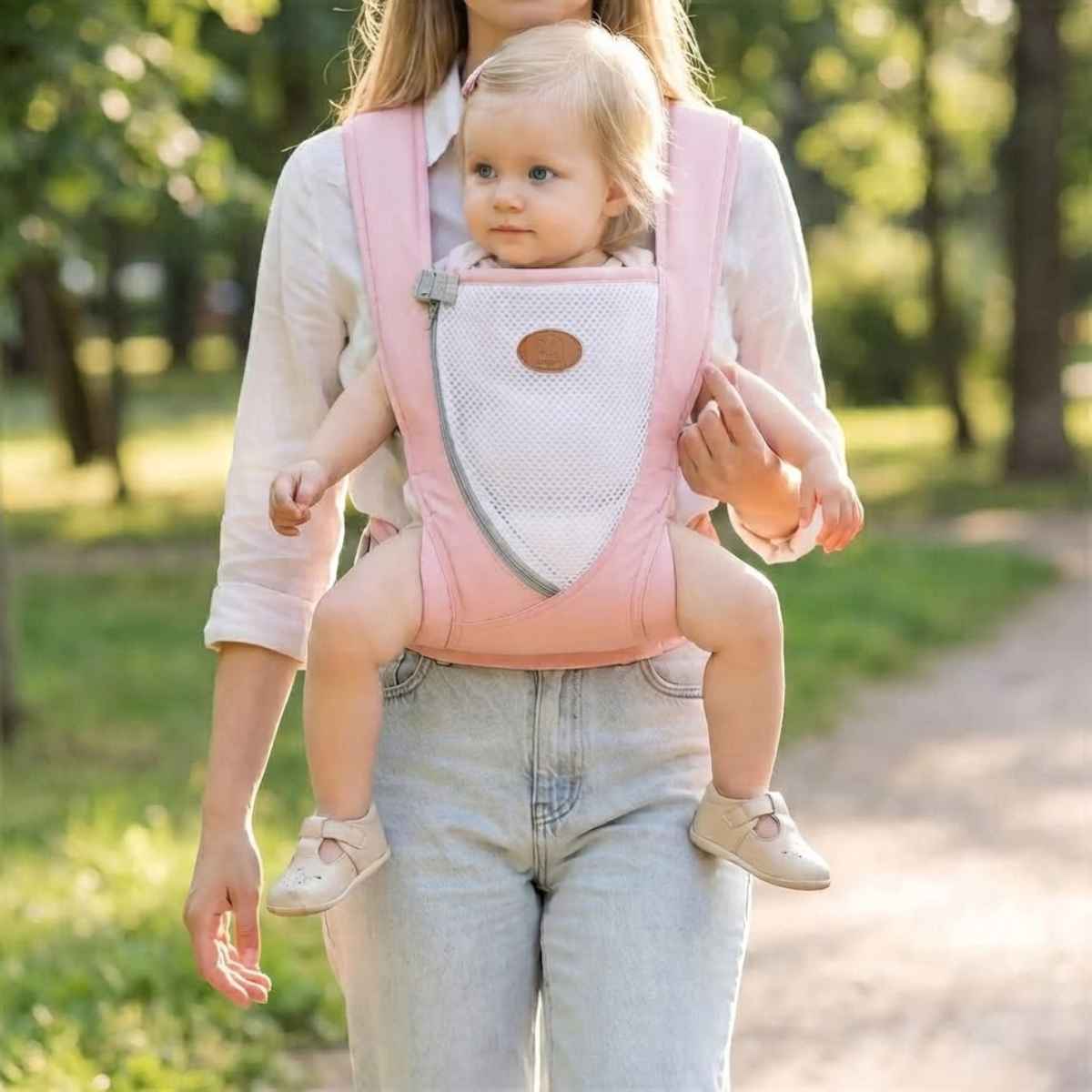 Porte-bébé croisé dans le dos rose avec bretelles larges et panneau en maille, porté face vers l’avant dans un parc