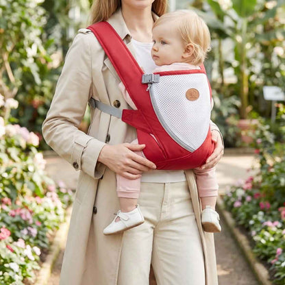 Porte-bébé croisé dans le dos rouge avec bretelles larges et panneau en maille, porté face au porteur dans un jardin
