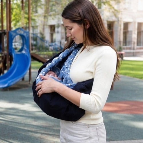 Porte bébé hamac bleu marine avec contour rembourré et sangle réglable, utilisé près d’une aire de jeux