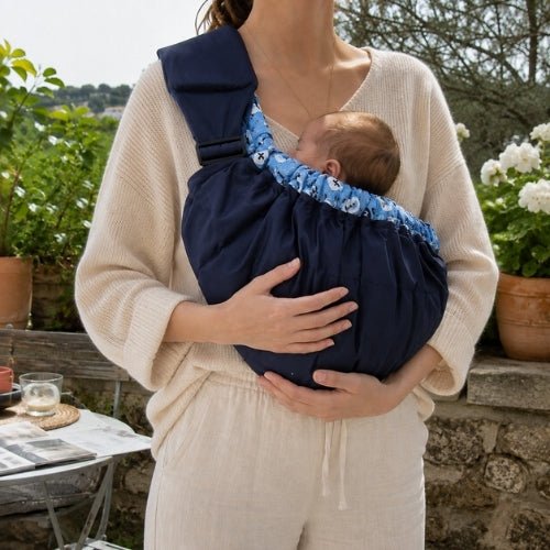 Porte bébé hamac bleu marine avec contour rembourré et sangle réglable, utilisé sur une terrasse