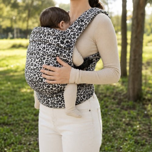 Porte bebe leopard noir et blanc porté face à face dans un parc