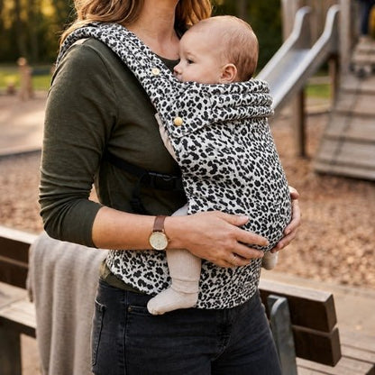 Porte bebe leopard noir et blanc porté face à face près d'une aire de jeux