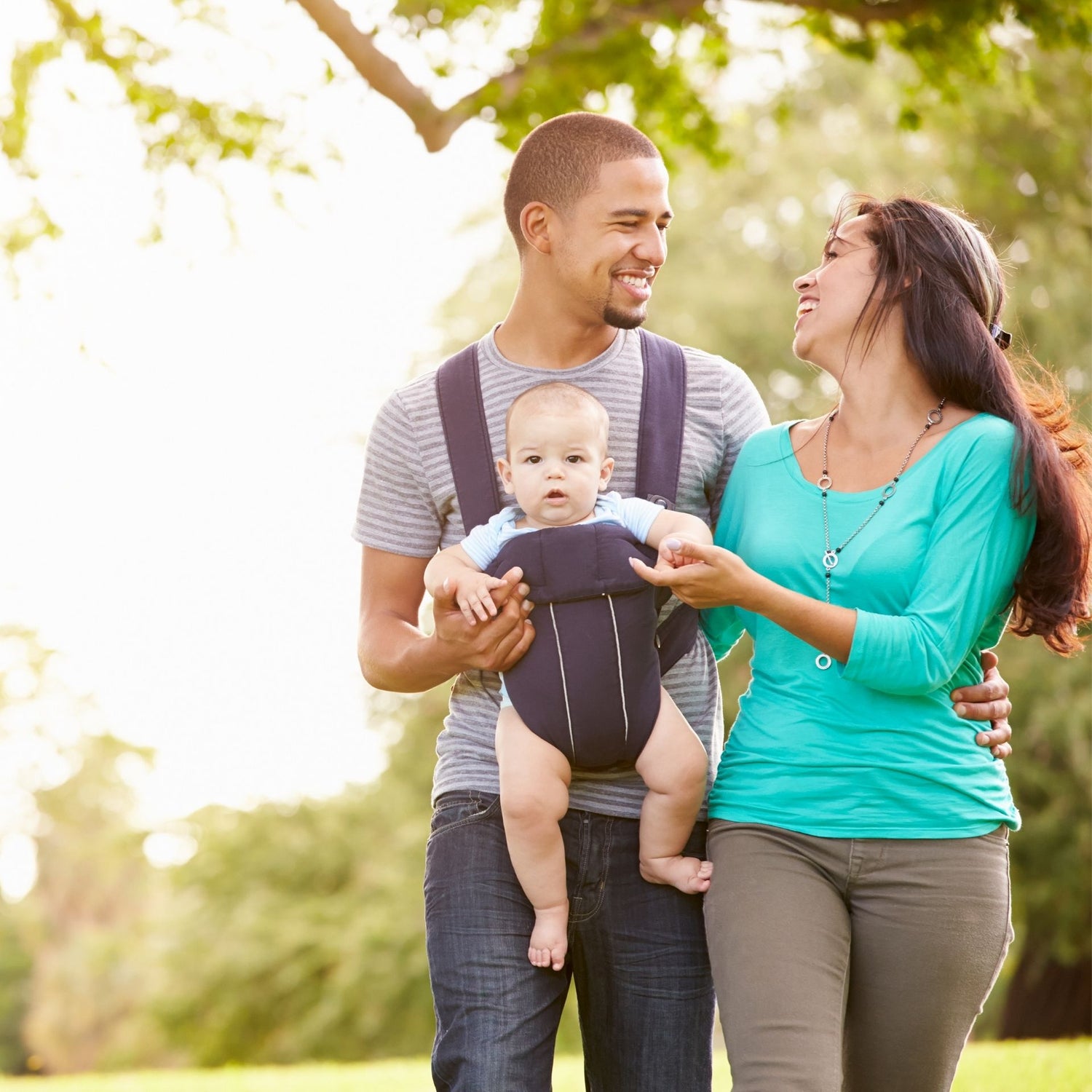 Papa portant un enfant dans un porte-bébé lors d’une balade en plein air avec la maman, moment familial joyeux