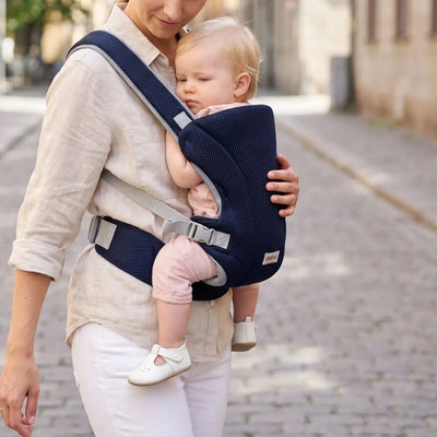 Porte-bébé mesh bleu marine avec bretelles croisées et format léger, porté face au porteur en ville