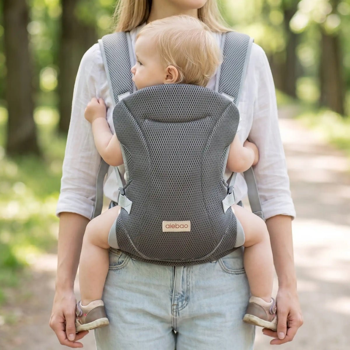 Porte-bébé mesh gris avec bretelles croisées et format léger, porté face vers l’avant dans un parc