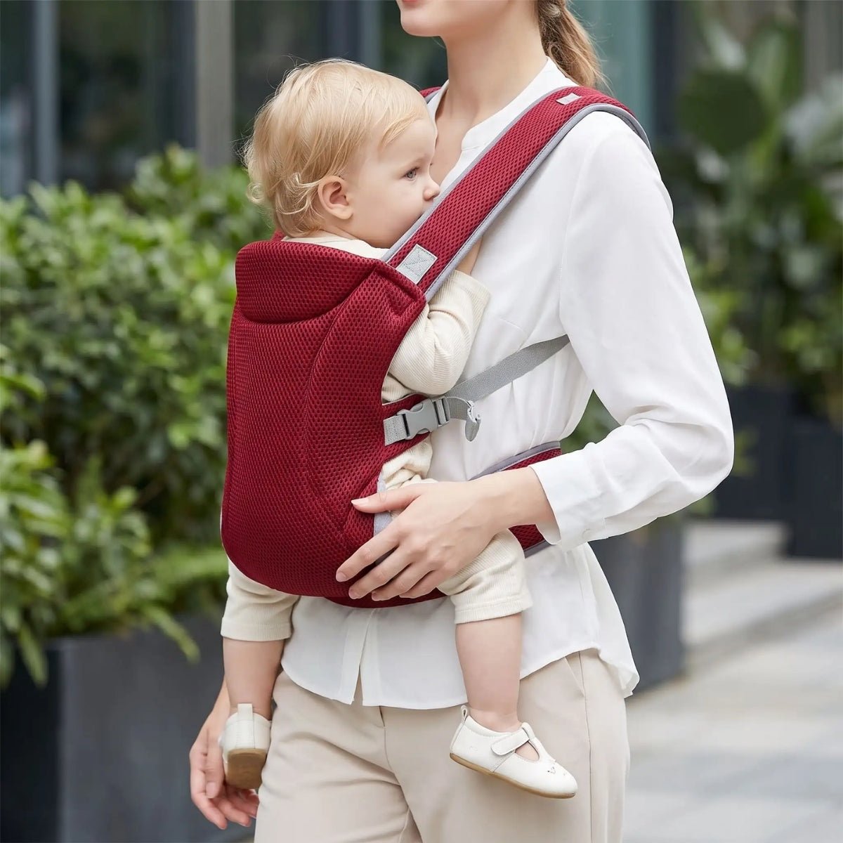 Porte-bébé mesh rouge avec bretelles croisées et format léger, porté face au porteur en extérieur