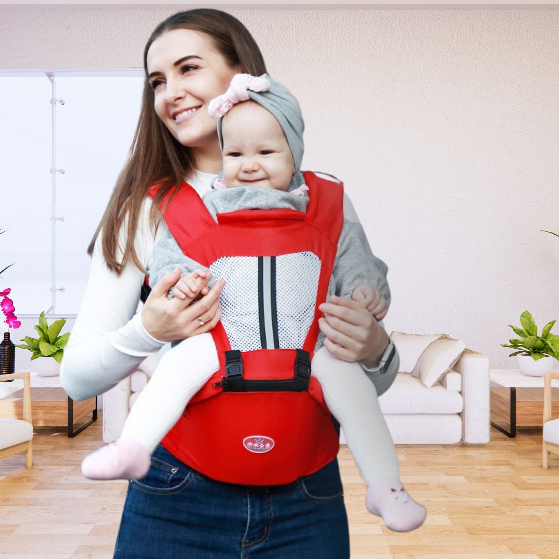 Maman souriante portant son enfant dans un porte-bébé rouge ergonomique à l’intérieur d’un salon lumineux