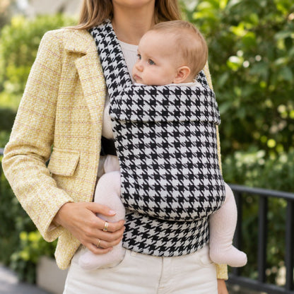 Porte-bébé pied-de-poule noir et blanc en coton, porté en ventral à l’extérieur avec veste jaune