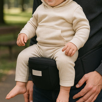 Bébé assis sur un porte bébé noir à repose-hanche intégré, porté par un adulte en extérieur