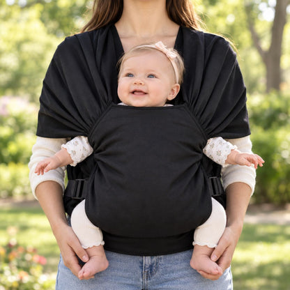 Porte-bébé sans nœud noir vu de face, avec bébé installé face au porteur dans un panneau textile enveloppant