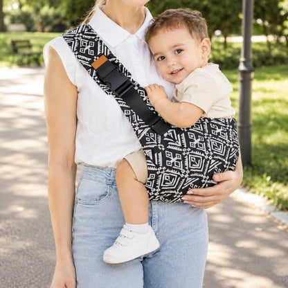 Porte-bébé souple à une épaule noir et blanc à motif géométrique, port latéral dans un parc