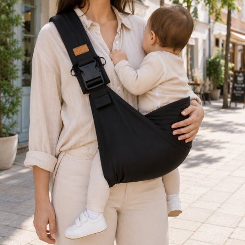 Porte-bébé souple à une épaule noir avec boucle réglable, port latéral dans une rue