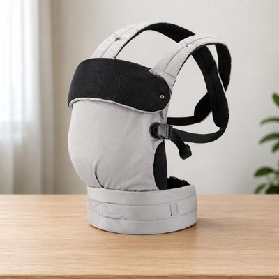 Porte bébé ventral et dorsal gris avec bretelles croisées, présenté seul sur une table