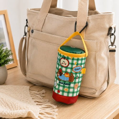 Sac à carreaux pour biberon à motif chien vert placé près d’un sac à langer