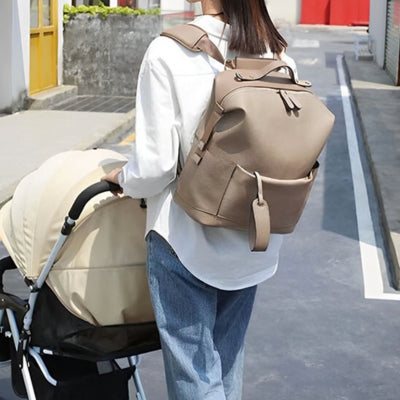 Sac à dos à langer camel, porté par une maman et fixé à la poussette pour un transport pratique et mains libres