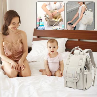 Une maman souriante avec son bébé sur un lit, avec un sac à dos à langer gris offrant une organisation optimale des affaires essentielles