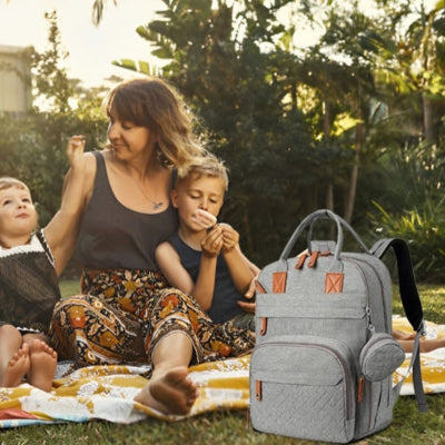 Sac à dos à langer gris SacDouillet™ en plein air avec une famille, montrant son design pratique et fonctionnel pour les parents