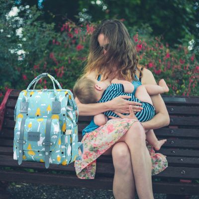 Sac à dos à langer VertZen vert clair posé sur un banc, avec une maman allaitant confortablement son bébé en plein air