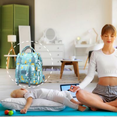 Sac à dos à langer VertZen vert clair placé dans une salle de méditation, avec une maman faisant du yoga près de son bébé endormi