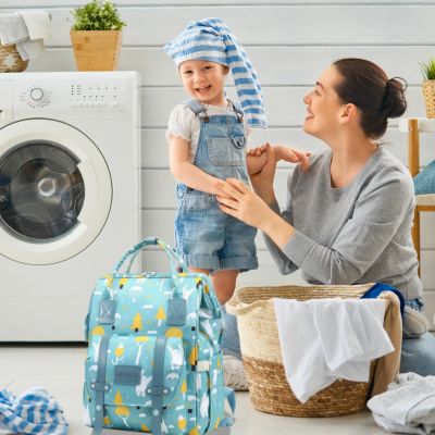 Sac à dos à langer VertZen vert clair posé dans une buanderie, avec une maman souriante et son enfant pliant le linge