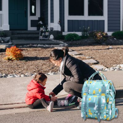 Sac à dos à langer VertZen vert clair posé à côté d'une maman et son enfant lors d'une sortie à l'extérieur pour jouer