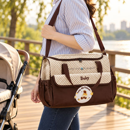 Vue trois quarts d'un sac à langer à pois marron et crème, décoré d'un écusson ourson, avec deux anses et une bandoulière portée à l'épaule