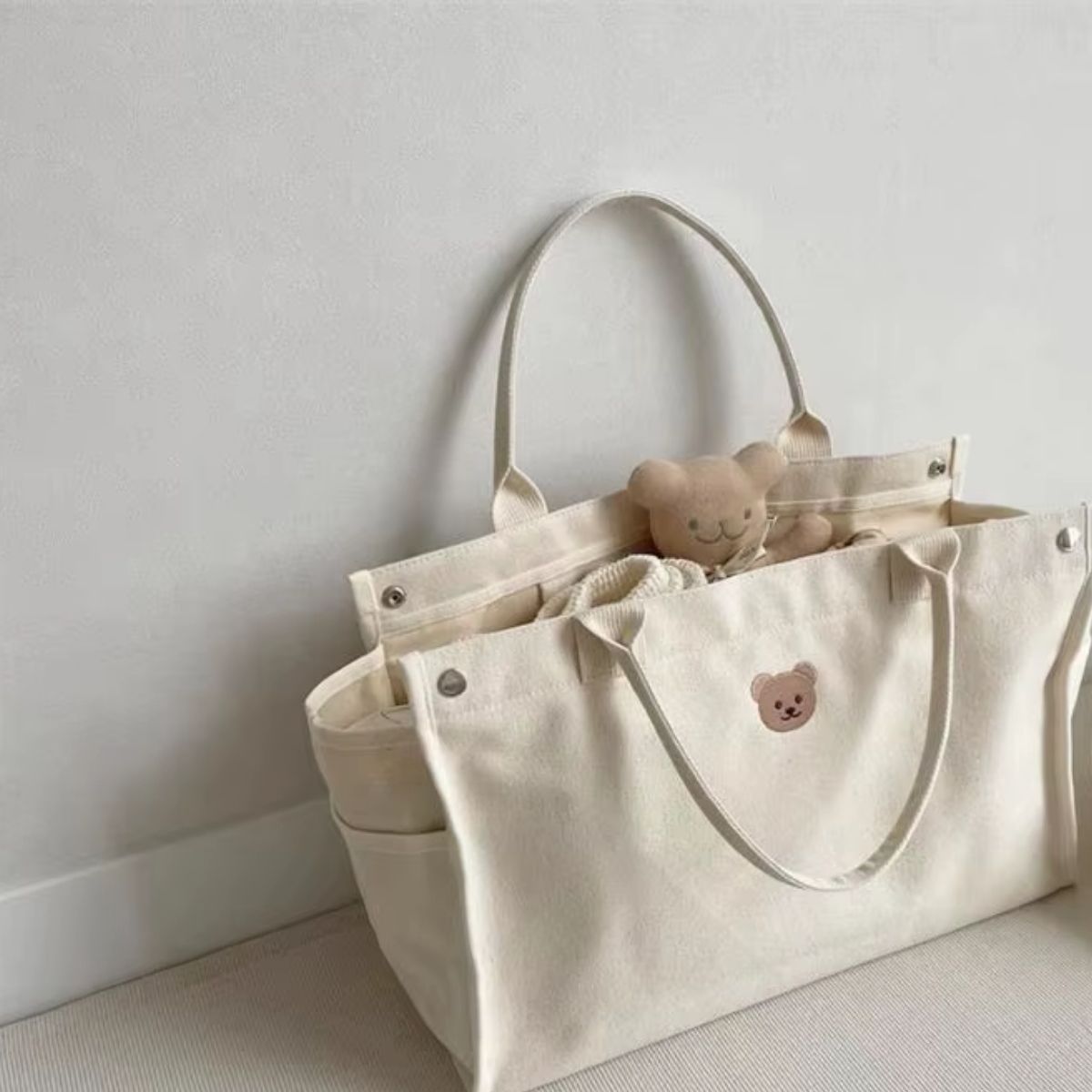 Sac a langer bebe beige posé au sol, ouvert avec peluche et affaires de bébé