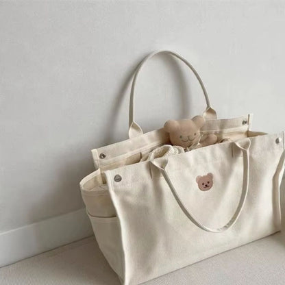 Sac a langer bebe beige posé au sol, ouvert avec peluche et affaires de bébé