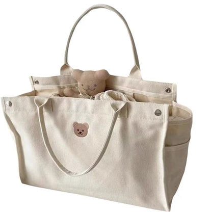 Sac a langer bebe beige avec motif ourson, ouvert et rempli d’accessoires pour bébé