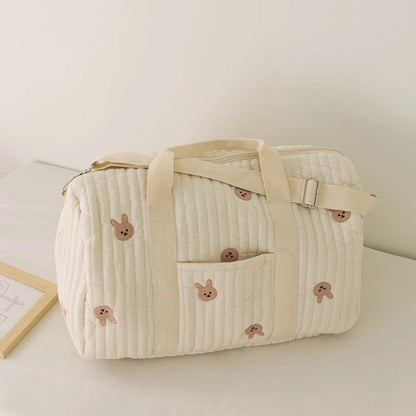sac a langer bebe lapins brodés beige, posé sur une table blanche