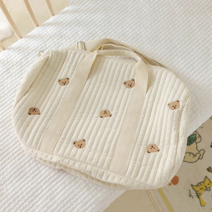 sac a langer bebe oursons brodés beige, posé sur un lit matelassé blanc