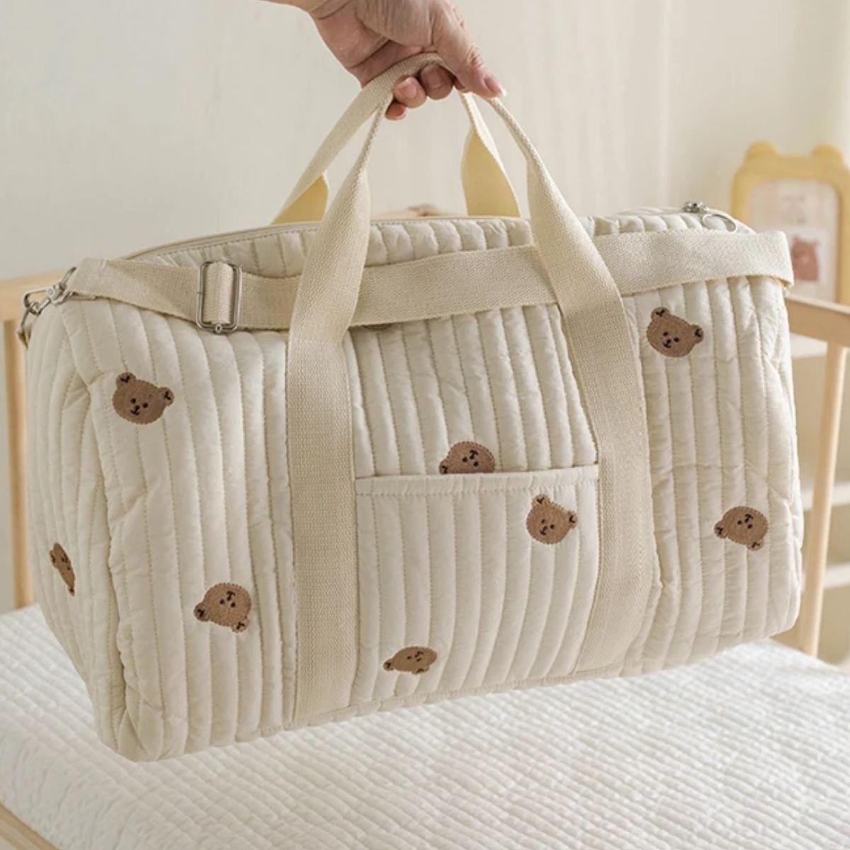 sac a langer bebe oursons brodés beige, porté à la main au-dessus du lit bébé