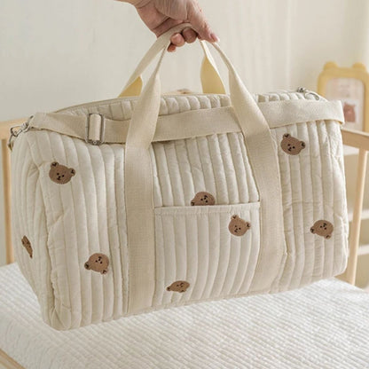 sac a langer bebe oursons brodés beige, porté à la main au-dessus du lit bébé
