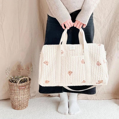 sac a langer bebe oursons brodés beige porté à la main devant un mur neutre