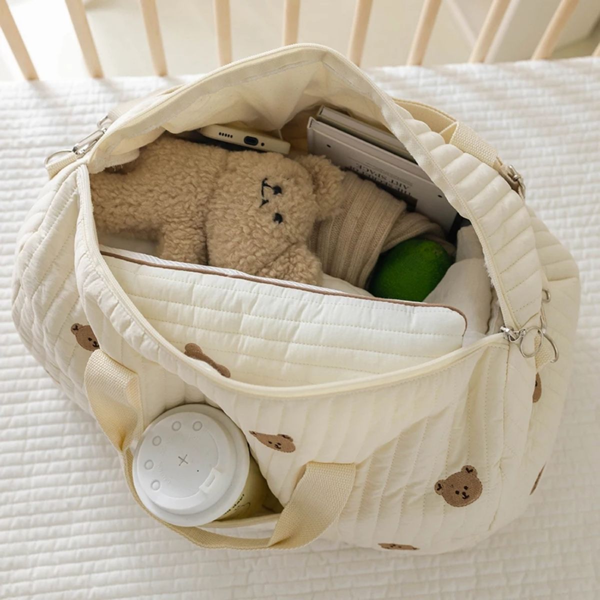 sac a langer bebe oursons brodés ouvert avec jouet, vêtements et accessoires rangés à l’intérieur