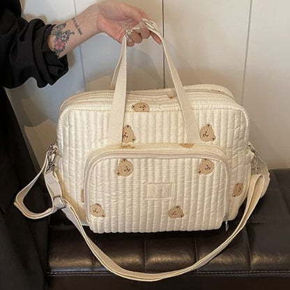 Sac a langer crème à motifs oursons posé sur banc, double poignée et tissu matelassé visibles