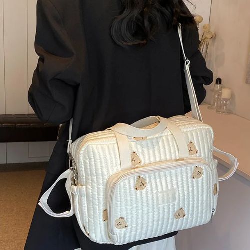  Sac a langer crème à broderies oursons porté dans le dos, bandoulière ajustée sur manteau noir.

