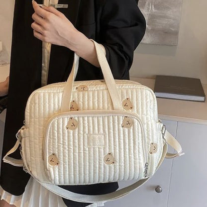 Sac a langer crème avec oursons brodés tenu à la main, devant un bureau et mur clair