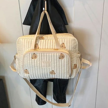 Sac a langer ourson suspendu sur un cintre, anse double et broderies visibles