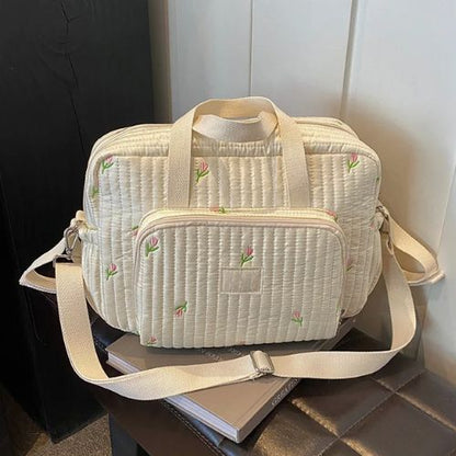 Sac a langer fleuri crème matelassé posé sur un livre, broderies tulipes visibles à l’avant