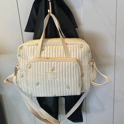 Sac a langer fleuri suspendu contre un mur, tissu crème matelassé avec petites fleurs brodées