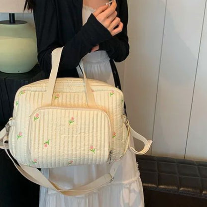 Femme en robe blanche tenant un sac a langer fleuri par les anses, ambiance douce et lumineuse