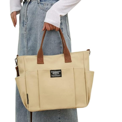 Sac a langer compact kaki porté à la main par une femme en jean, format compact élégant