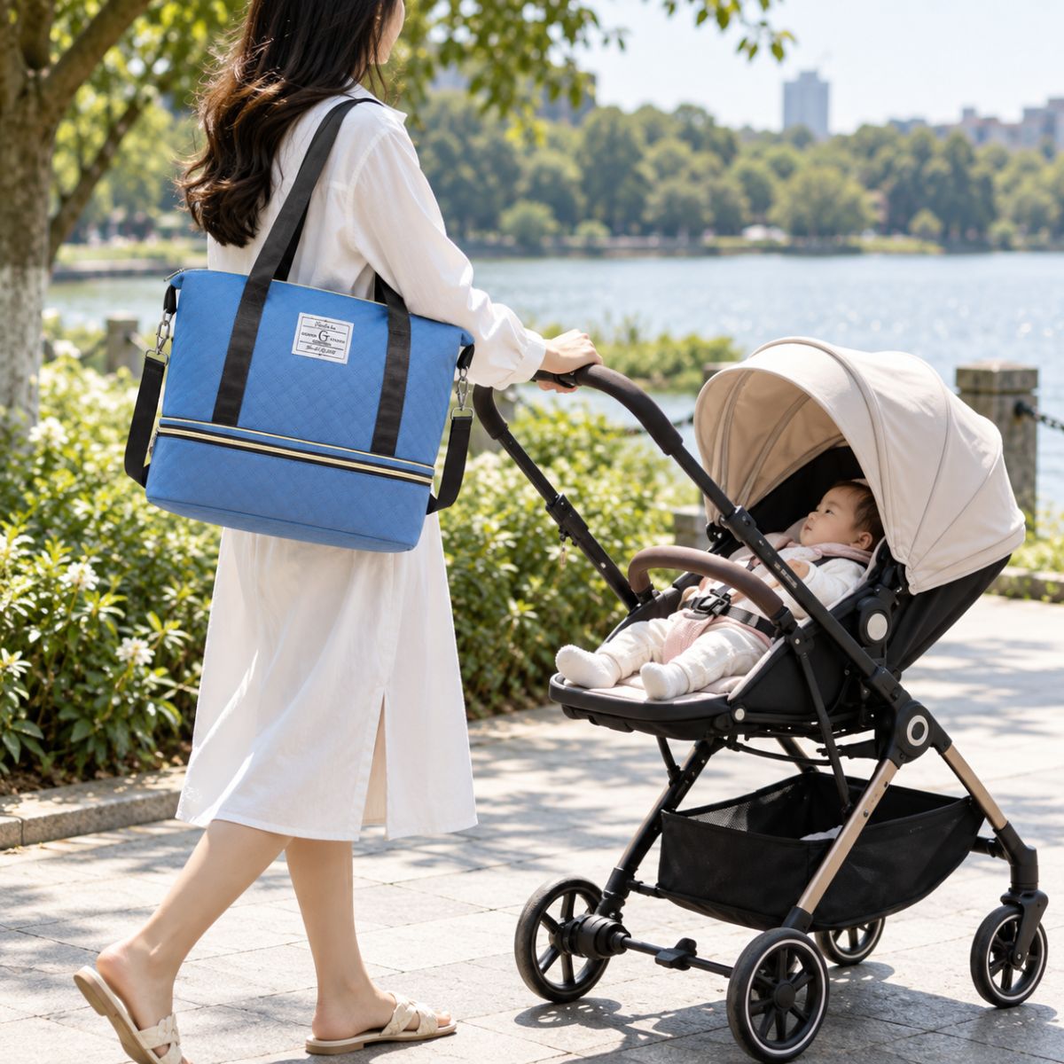 Sac à langer extensible bleu porté à l’épaule par une femme près d’une poussette au bord d’un lac