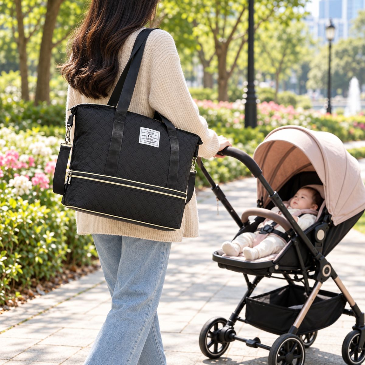 Sac à langer extensible noir porté à l’épaule par une femme près d’une poussette dans un parc
